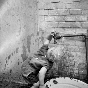 823282 Afbeelding van een peuter uit de kindercrêche, drinkend bij een kraan op het binnenterrein van het Klooster ...